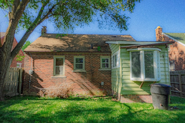 back of property with brick siding, a lawn, and fence