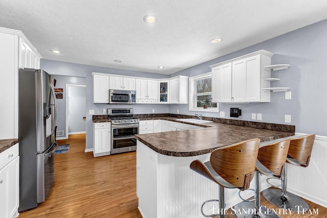 kitchen with a peninsula, appliances with stainless steel finishes, dark countertops, and a sink