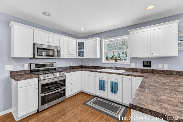 kitchen featuring dark countertops, appliances with stainless steel finishes, wood finished floors, white cabinetry, and a sink