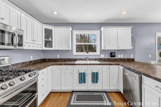 kitchen with stainless steel appliances, light wood-style floors, a sink, and white cabinets