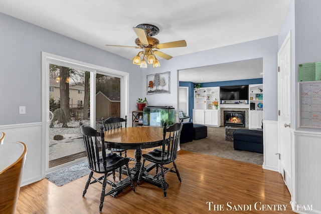 dining space with built in shelves, a glass covered fireplace, wainscoting, and wood finished floors