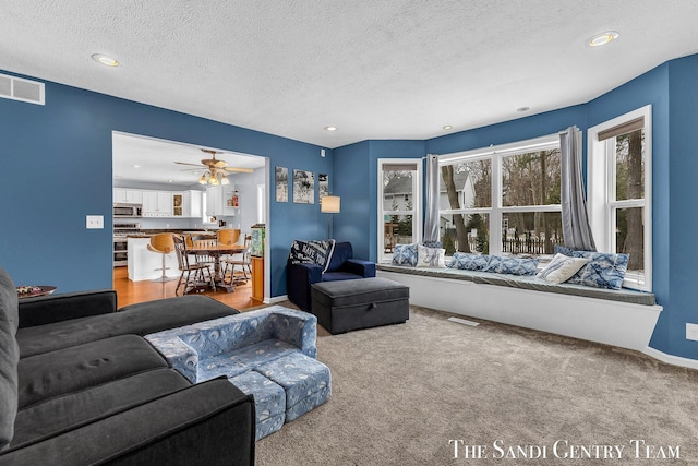 living room with a textured ceiling, light carpet, visible vents, and recessed lighting