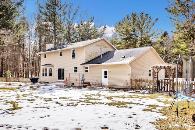 snow covered property featuring a trampoline, a chimney, entry steps, a gate, and fence