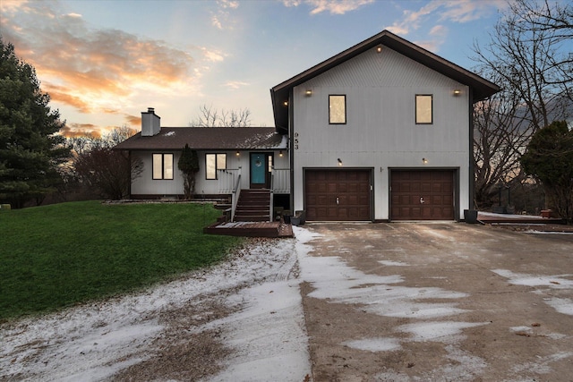 tri-level home featuring driveway, an attached garage, a chimney, and a lawn