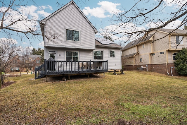 rear view of property with solar panels, fence, a deck, and a lawn