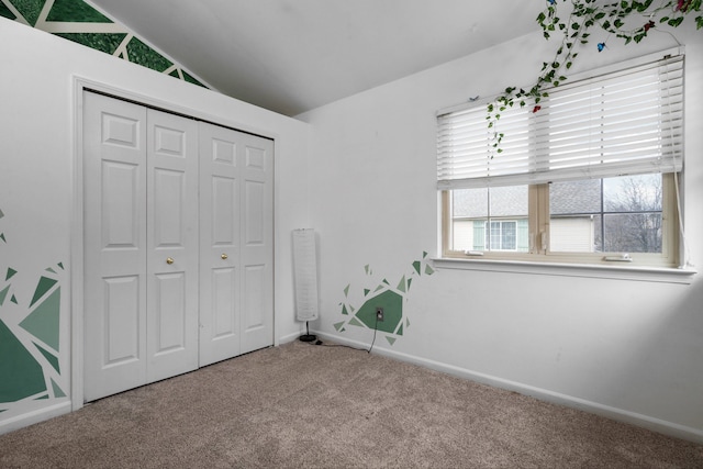 unfurnished bedroom featuring vaulted ceiling, a closet, carpet, and baseboards