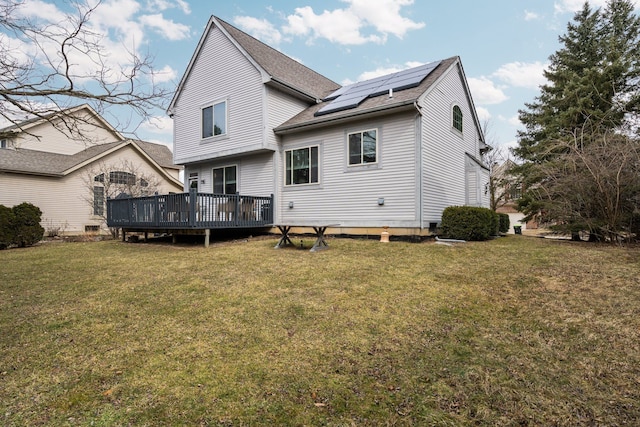 back of property with a wooden deck, roof with shingles, solar panels, and a yard