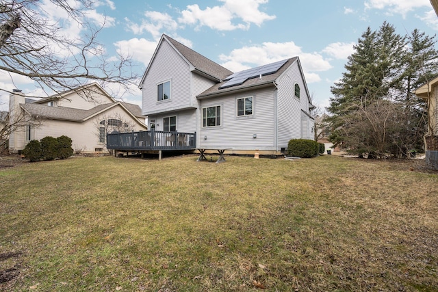 rear view of property with solar panels, a yard, roof with shingles, and a wooden deck