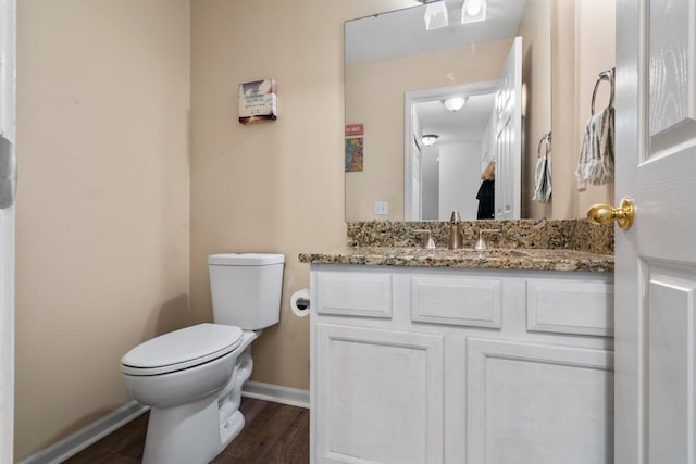 half bath featuring baseboards, vanity, toilet, and wood finished floors