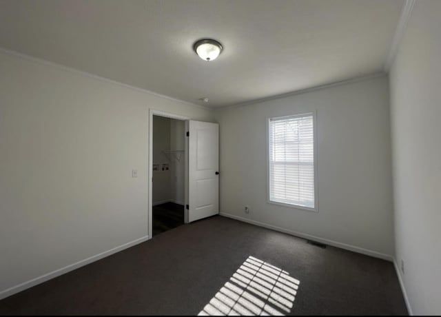 empty room with visible vents, baseboards, dark colored carpet, and crown molding