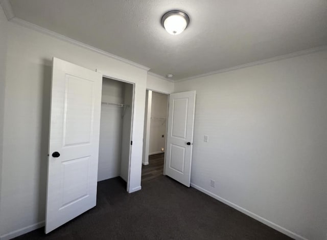 unfurnished bedroom with dark colored carpet, ornamental molding, a closet, and baseboards