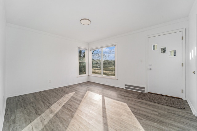 interior space with baseboards, wood finished floors, visible vents, and crown molding