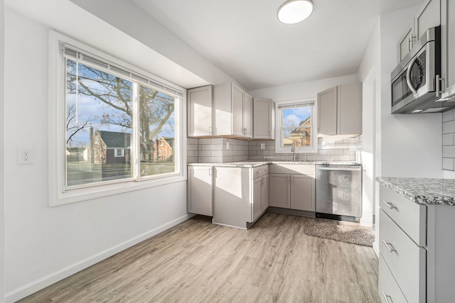 kitchen with light wood finished floors, appliances with stainless steel finishes, gray cabinets, and backsplash