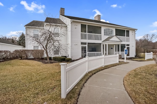 back of house featuring a fenced front yard, a yard, a chimney, and a balcony