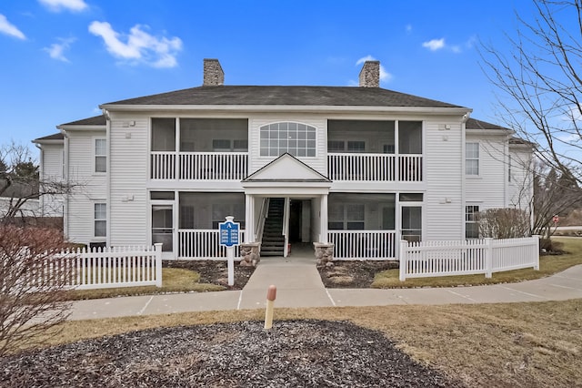 rear view of house with a sunroom, fence, a chimney, and stairs