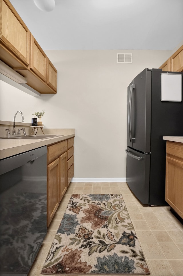 kitchen featuring visible vents, dishwasher, freestanding refrigerator, light countertops, and a sink