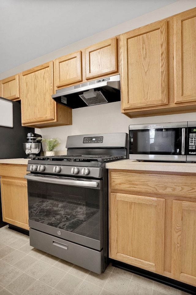 kitchen with stainless steel appliances, light brown cabinetry, light countertops, and under cabinet range hood