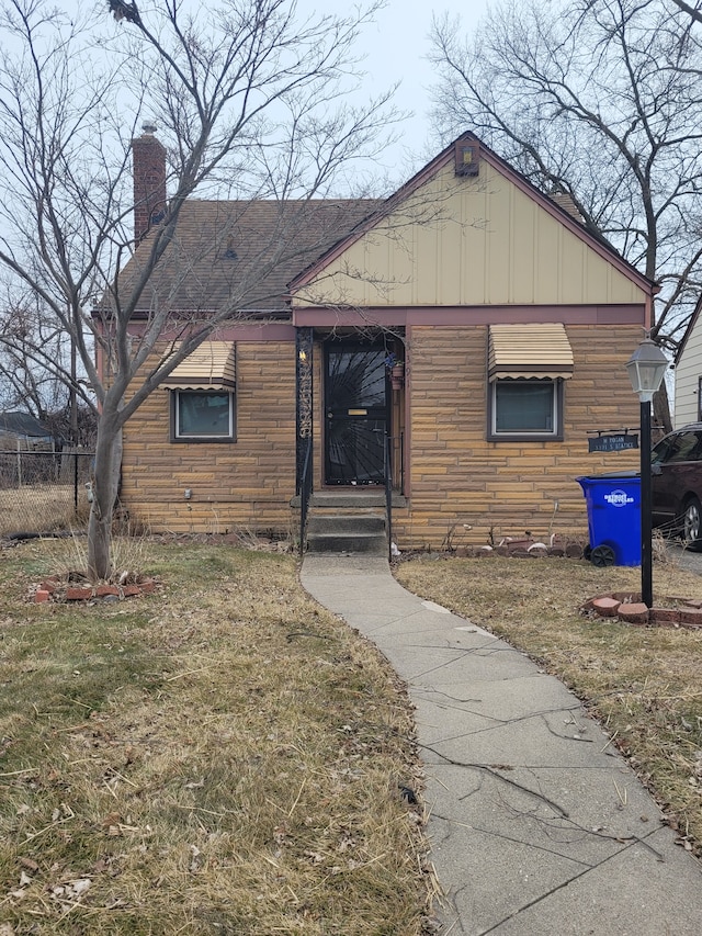 view of front facade with board and batten siding, stone siding, fence, and a chimney