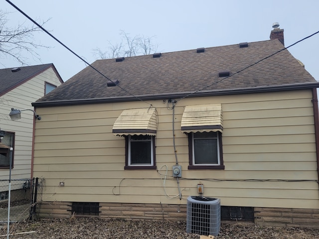 exterior space with a shingled roof, a chimney, cooling unit, and fence