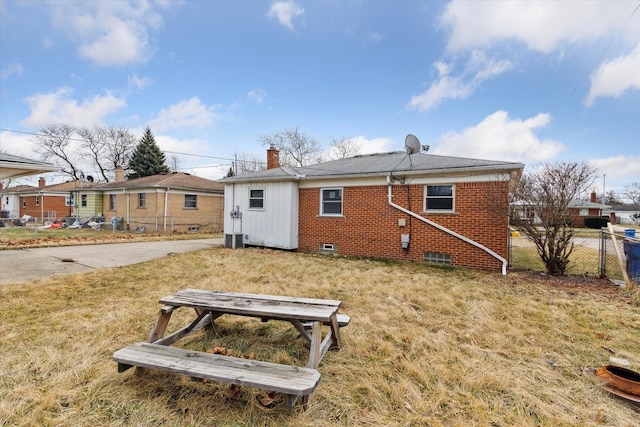 rear view of house with brick siding, fence, a chimney, and a lawn