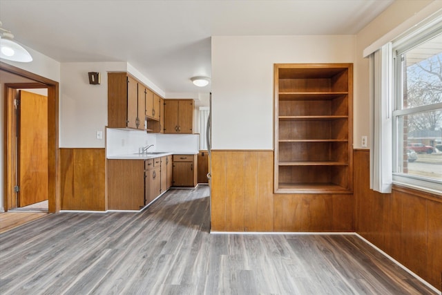 kitchen with brown cabinets, light countertops, a wainscoted wall, and wood walls