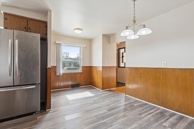 kitchen with brown cabinets, a notable chandelier, freestanding refrigerator, wainscoting, and wood finished floors