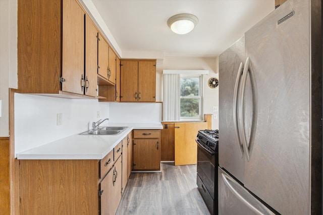 kitchen with black range with gas cooktop, a sink, light countertops, freestanding refrigerator, and light wood finished floors