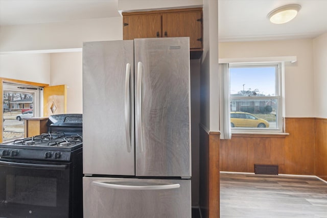 kitchen featuring visible vents, wainscoting, freestanding refrigerator, black range with gas stovetop, and wood walls