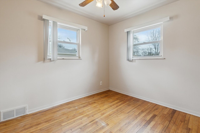 empty room featuring a wealth of natural light, light wood-type flooring, visible vents, and baseboards