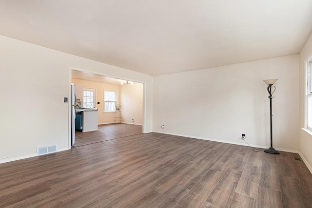 unfurnished living room with baseboards, visible vents, and dark wood-style flooring