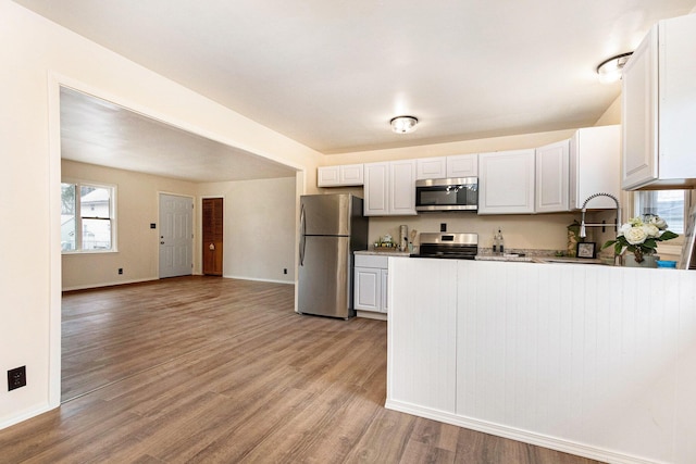 kitchen featuring light wood-type flooring, stainless steel appliances, a peninsula, and white cabinets