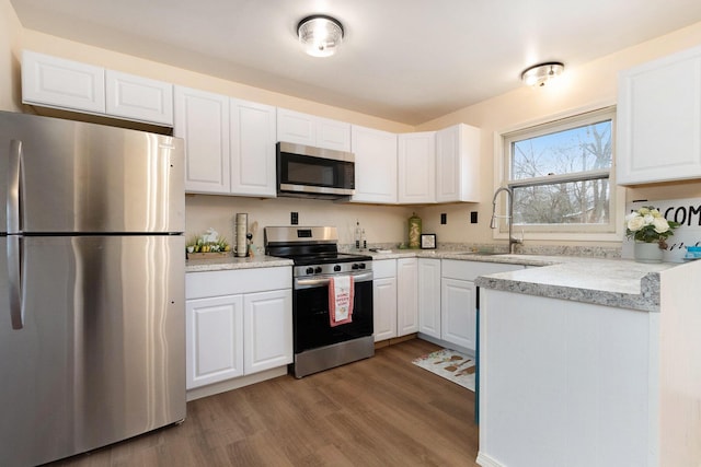 kitchen with light stone counters, wood finished floors, a sink, appliances with stainless steel finishes, and white cabinetry