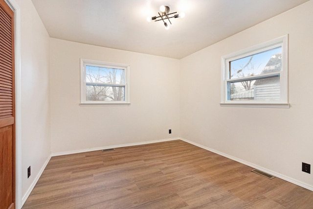 spare room featuring wood finished floors, visible vents, and baseboards