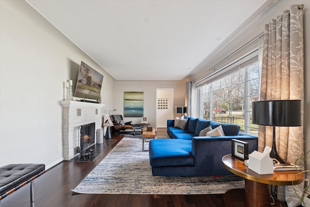 living room featuring a brick fireplace, wood finished floors, and baseboards