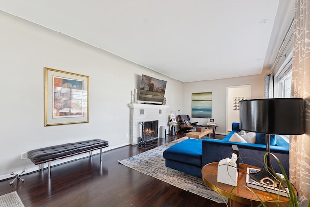 living area with baseboards, a brick fireplace, and wood finished floors