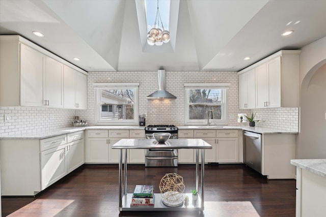 kitchen featuring backsplash, wall chimney range hood, dark wood finished floors, appliances with stainless steel finishes, and a sink