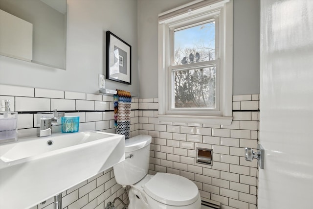 half bath with a sink, tile walls, toilet, and a baseboard radiator