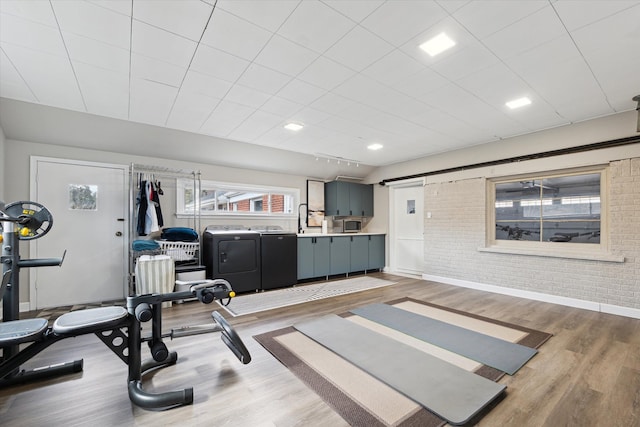 exercise area with light wood-style flooring, a sink, washing machine and dryer, brick wall, and baseboards