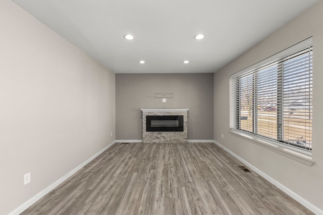 unfurnished living room with visible vents, wood finished floors, recessed lighting, a stone fireplace, and baseboards