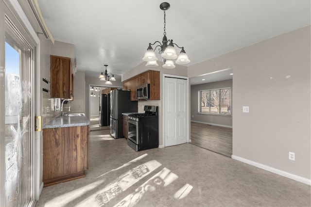 kitchen featuring baseboards, appliances with stainless steel finishes, an inviting chandelier, brown cabinetry, and a sink