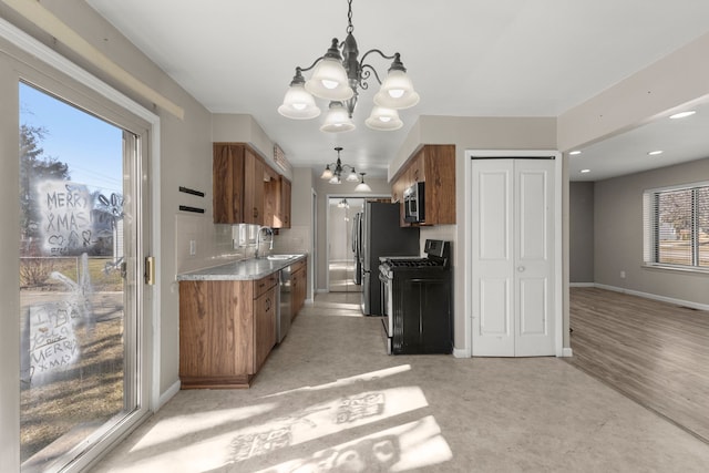 kitchen with a sink, an inviting chandelier, brown cabinetry, and stainless steel appliances