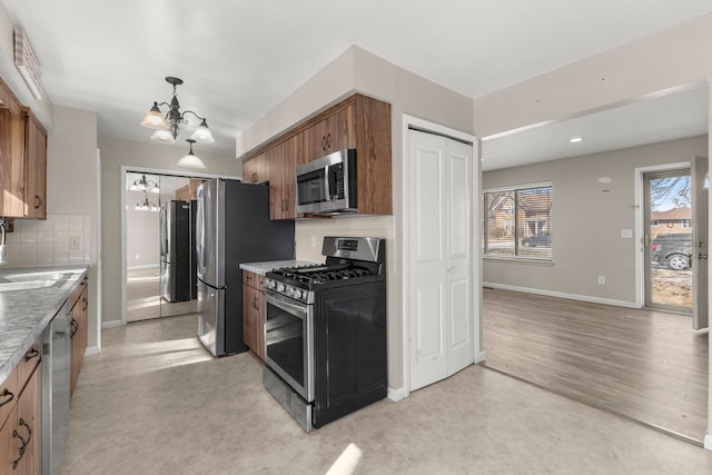 kitchen featuring baseboards, an inviting chandelier, a sink, appliances with stainless steel finishes, and tasteful backsplash