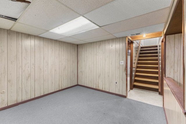 finished basement with stairway, carpet, visible vents, and wood walls