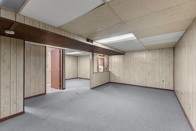 finished below grade area featuring wooden walls, a drop ceiling, visible vents, and carpet floors