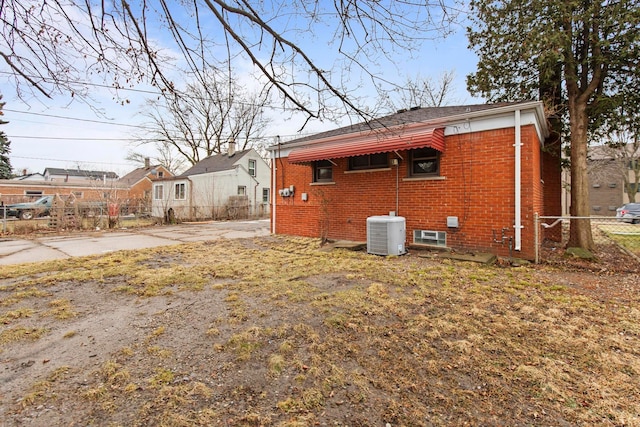 rear view of property with cooling unit, brick siding, and fence