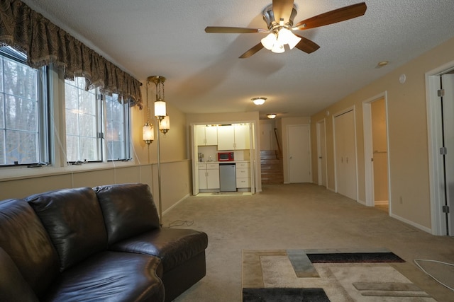 living area with a textured ceiling, baseboards, a ceiling fan, and light colored carpet