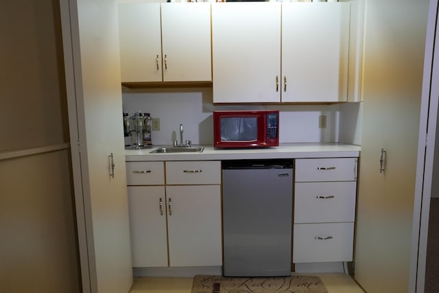 kitchen with white cabinetry, light countertops, a sink, and fridge