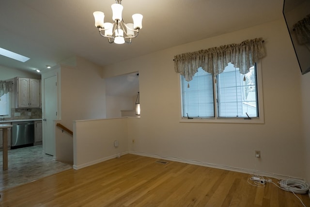 unfurnished dining area with a chandelier, a skylight, baseboards, and light wood finished floors