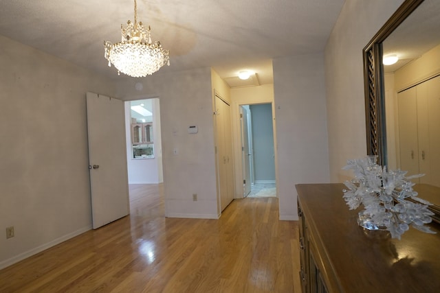 corridor featuring light wood-style floors, baseboards, and a notable chandelier