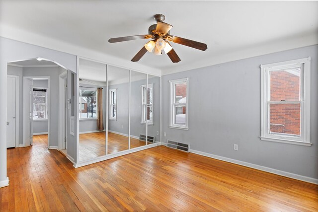 unfurnished bedroom with visible vents, wood-type flooring, arched walkways, and baseboards